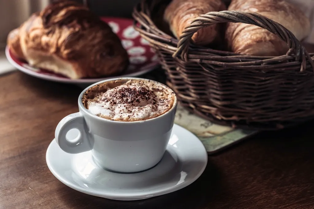 capuchino en taza blanca junto a una cesta de cruasanes