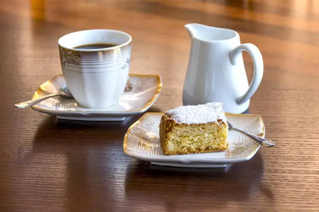 porción de bizcocho junto a una taza de café y una jarrita de leche